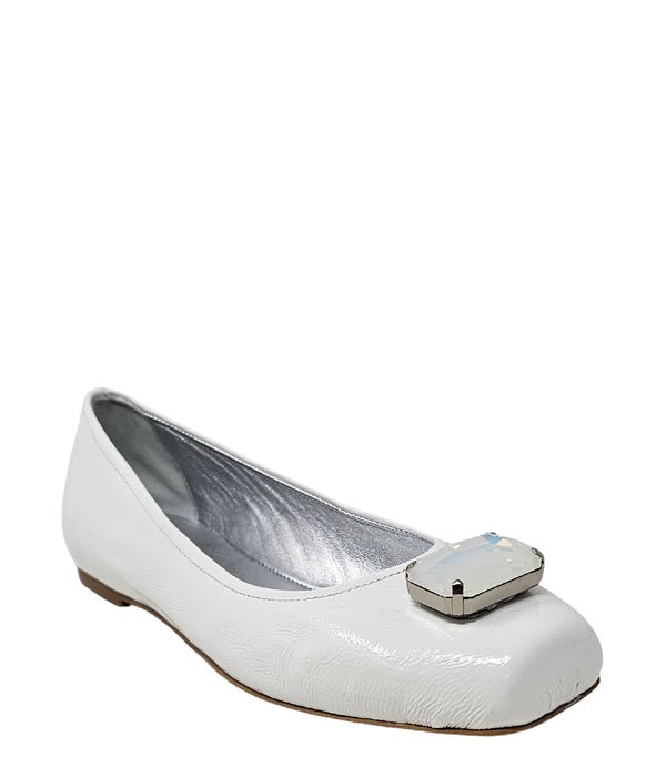 Four-angle view of a women's flat shoe with a glossy leather finish, rounded square toe, and a large faceted jewel embellishment at the toe. The shoe features a low-profile sole and a metallic-toned interior lining, displayed from side, angled, back, and