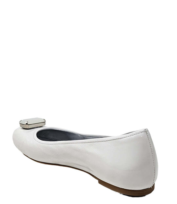 Four-angle view of a women's flat shoe with a glossy leather finish, rounded square toe, and a large faceted jewel embellishment at the toe. The shoe features a low-profile sole and a metallic-toned interior lining, displayed from side, angled, back, and