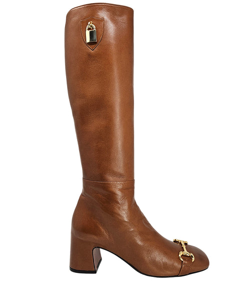 A tall leather boot with a block heel and rounded toe, featuring a metal horsebit-style detail at the front and a small metal padlock accent near the top of the shaft. Designed by Madison in Beverly Hills and handcrafted in Italy