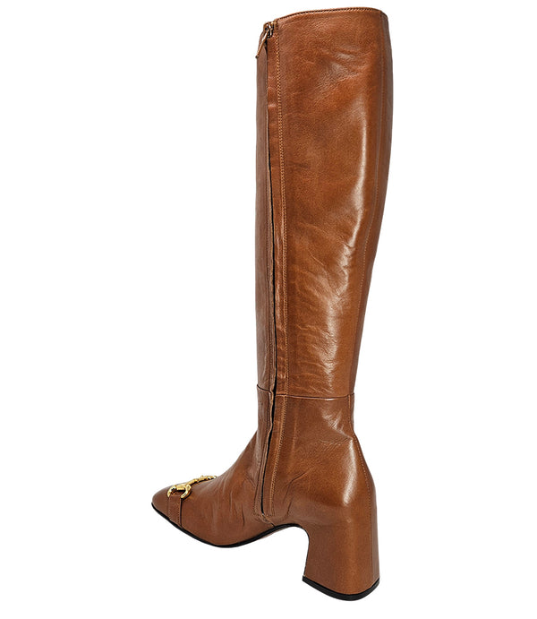 A tall leather boot with a block heel and rounded toe, featuring a metal horsebit-style detail at the front and a small metal padlock accent near the top of the shaft. Designed by Madison in Beverly Hills and handcrafted in Italy