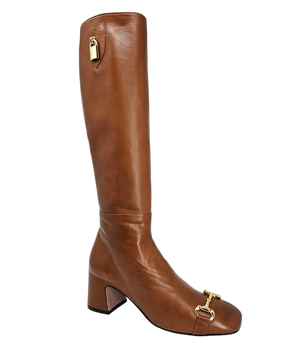 A tall leather boot with a block heel and rounded toe, featuring a metal horsebit-style detail at the front and a small metal padlock accent near the top of the shaft. Designed by Madison in Beverly Hills and handcrafted in Italy