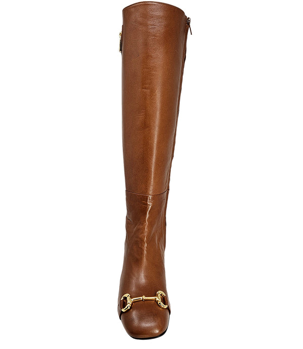 A tall leather boot with a block heel and rounded toe, featuring a metal horsebit-style detail at the front and a small metal padlock accent near the top of the shaft. Designed by Madison in Beverly Hills and handcrafted in Italy