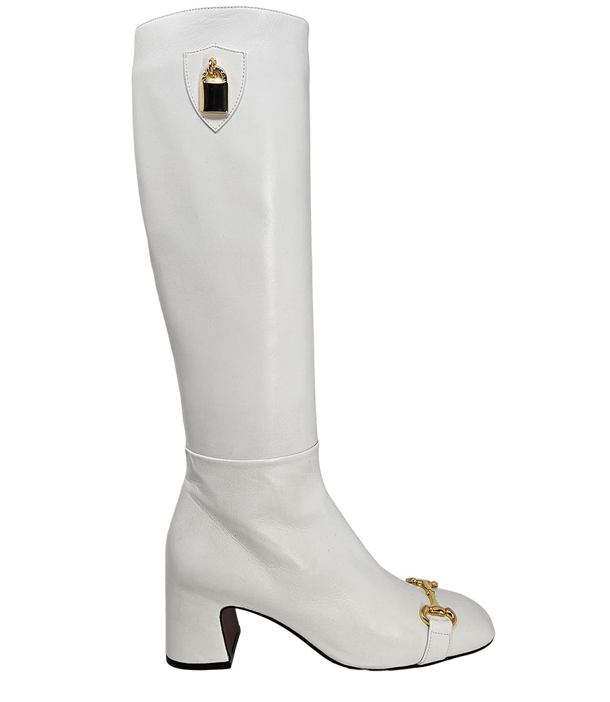 A tall leather boot with a block heel and rounded toe, featuring a metal horsebit-style detail at the front and a small metal padlock accent near the top of the shaft. Designed by Madison in Beverly Hills and handcrafted in Italy