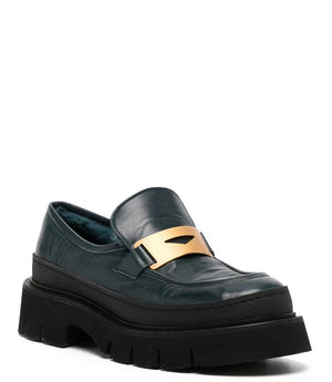 A leather loafer with an exaggerated lug sole and low-cut silhouette, featuring a wide strap with a geometric metal detail across the upper. Designed by Madison in Beverly Hills and handcrafted in Italy.