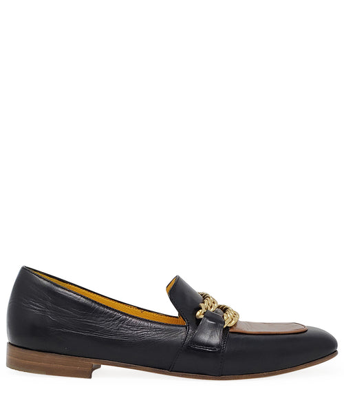 A leather loafer with a flat sole and rounded toe, featuring a contrasting vamp panel and dual chain accents across the upper. Designed by Madison in Beverly Hills and handcrafted in Italy.