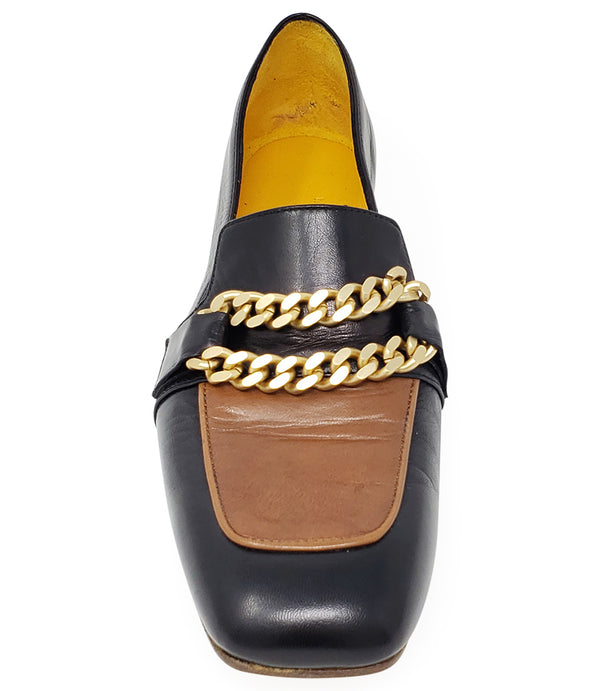 A leather loafer with a flat sole and rounded toe, featuring a contrasting vamp panel and dual chain accents across the upper. Designed by Madison in Beverly Hills and handcrafted in Italy.