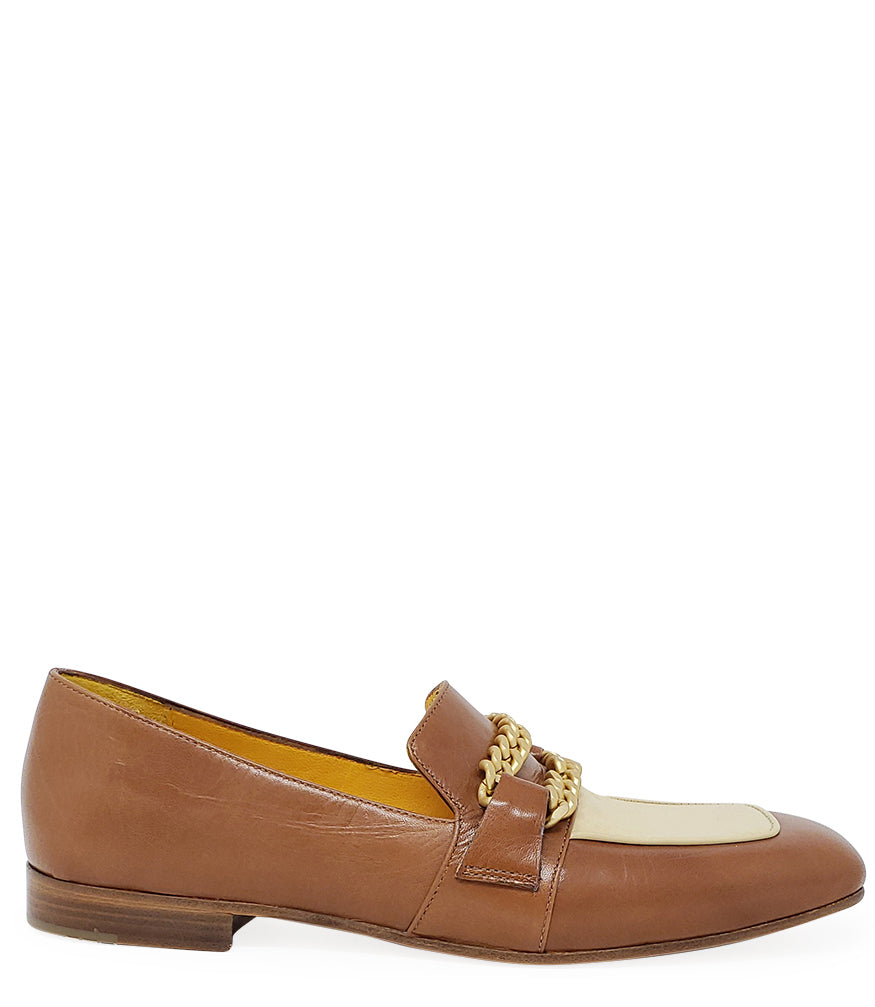 A leather loafer with a flat sole and rounded toe, featuring a contrasting vamp panel and dual chain accents across the upper. Designed by Madison in Beverly Hills and handcrafted in Italy.