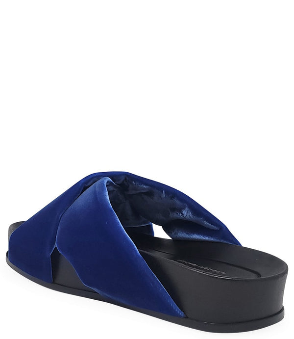 A handcrafted Italian open-toe flat sandal featuring a wide strap with a centered oval gemstone surrounded by circular studs, set on a molded footbed with a low platform sole."