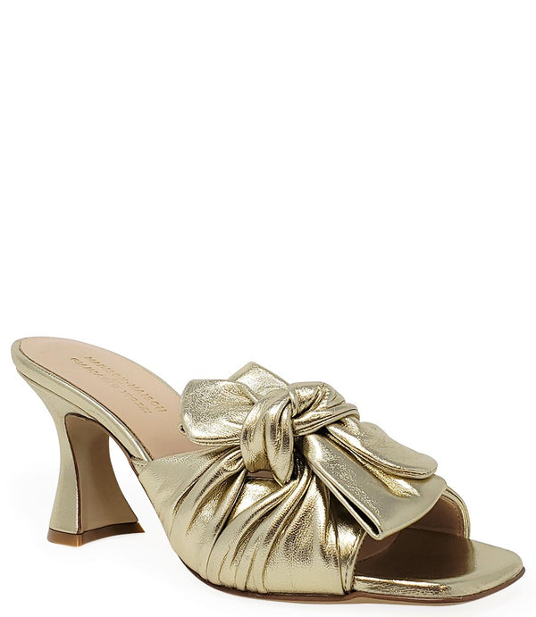 Open-toe mule handcrafted in Italy, featuring a metallic finish, wide vamp with a twisted bow detail, and a flared heel. Shown from multiple angles against a clean background