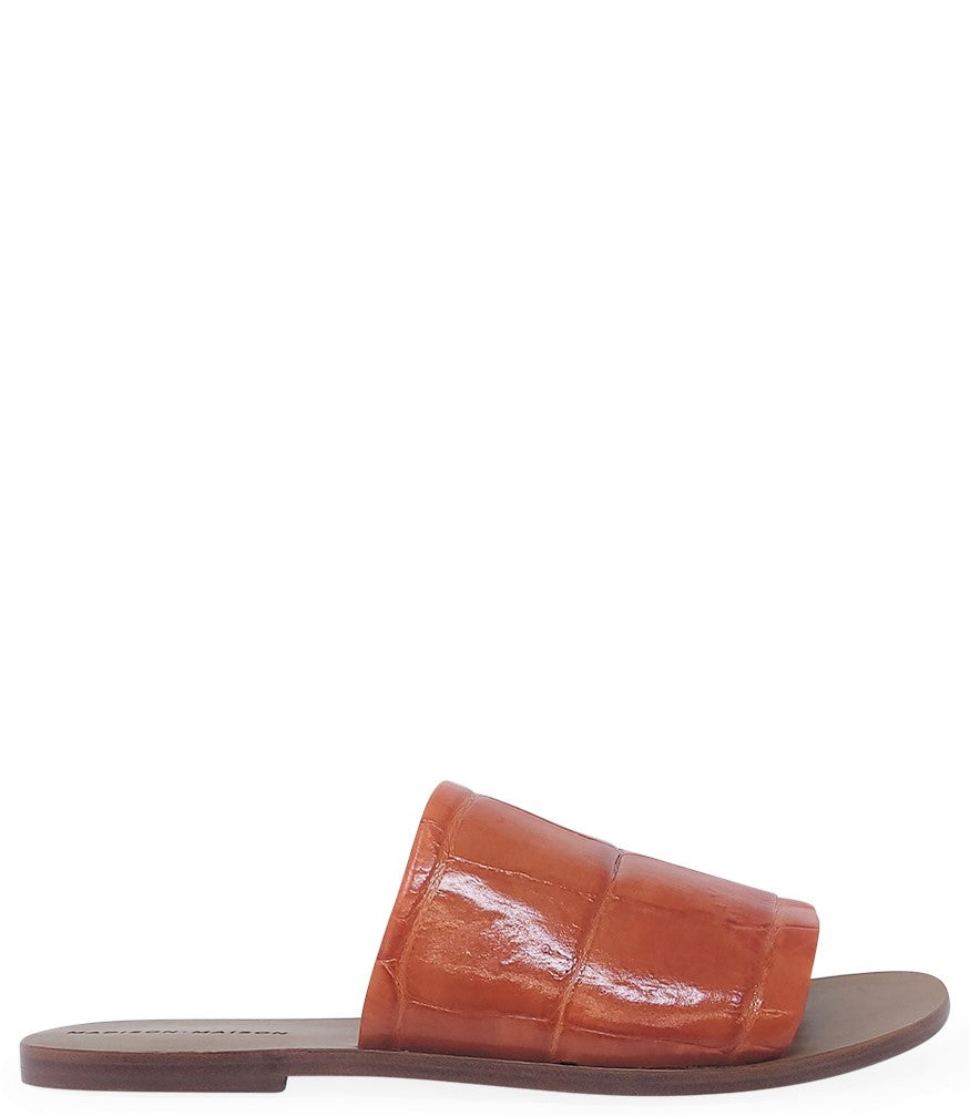 Handmade slide sandal crafted in Italy with a wide, textured band across the foot and a flat leather sole. Features a structured, embossed finish. Displayed from front and side angles against a clean background.