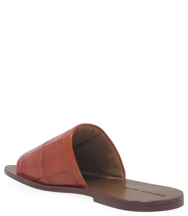 Handmade slide sandal crafted in Italy with a wide, textured band across the foot and a flat leather sole. Features a structured, embossed finish. Displayed from front and side angles against a clean background.