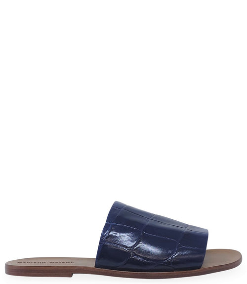 Handmade slide sandal crafted in Italy with a wide, textured band across the foot and a flat leather sole. Features a structured, embossed finish. Displayed from front and side angles against a clean background.