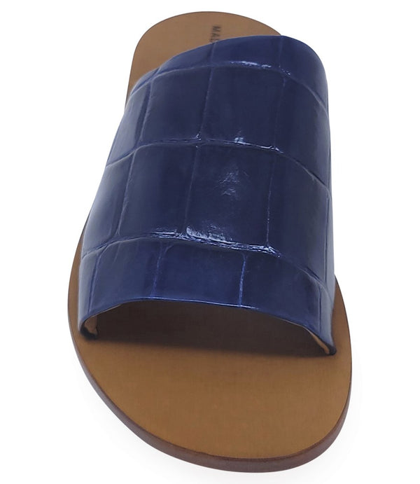 Handmade slide sandal crafted in Italy with a wide, textured band across the foot and a flat leather sole. Features a structured, embossed finish. Displayed from front and side angles against a clean background.