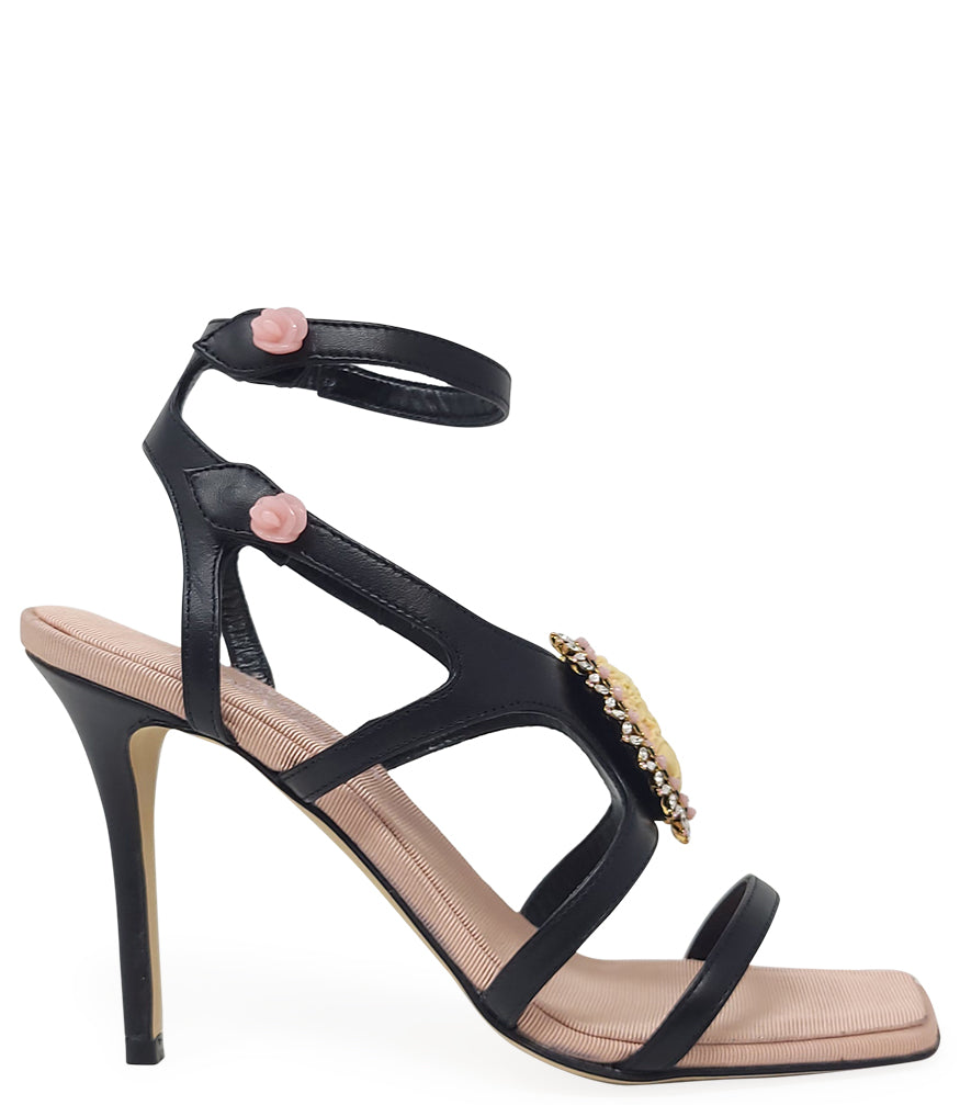 High-heeled sandal made in Italy with an open toe, strappy upper, and sculptural ankle strap secured by floral-shaped accents. Features a raised cameo embellishment with crystal trim on the instep. Presented from multiple angles against a clean background