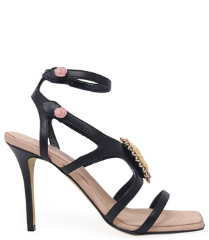 High-heeled sandal made in Italy with an open toe, strappy upper, and sculptural ankle strap secured by floral-shaped accents. Features a raised cameo embellishment with crystal trim on the instep. Presented from multiple angles against a clean background