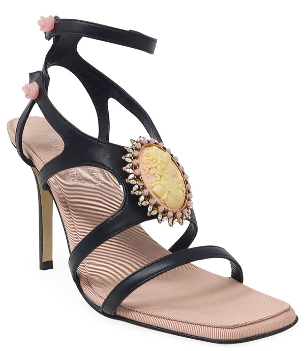 High-heeled sandal made in Italy with an open toe, strappy upper, and sculptural ankle strap secured by floral-shaped accents. Features a raised cameo embellishment with crystal trim on the instep. Presented from multiple angles against a clean background
