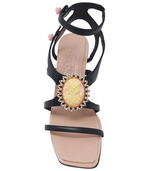 High-heeled sandal made in Italy with an open toe, strappy upper, and sculptural ankle strap secured by floral-shaped accents. Features a raised cameo embellishment with crystal trim on the instep. Presented from multiple angles against a clean background