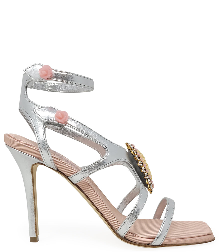 High-heeled sandal made in Italy with an open toe, strappy upper, and sculptural ankle strap secured by floral-shaped accents. Features a raised cameo embellishment with crystal trim on the instep. Presented from multiple angles against a clean background