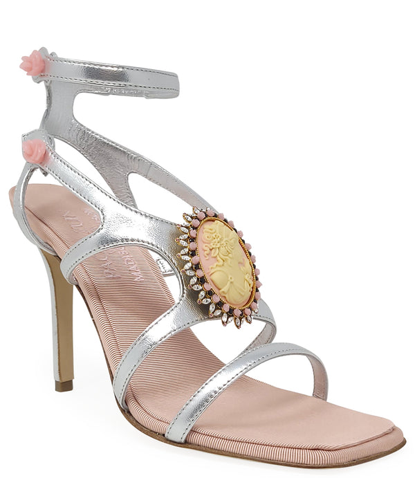 High-heeled sandal made in Italy with an open toe, strappy upper, and sculptural ankle strap secured by floral-shaped accents. Features a raised cameo embellishment with crystal trim on the instep. Presented from multiple angles against a clean background