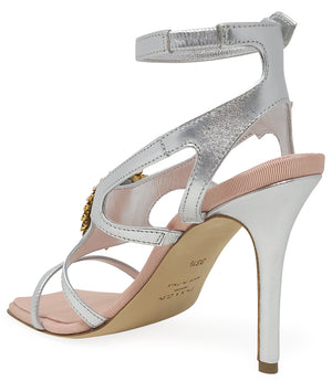 High-heeled sandal made in Italy with an open toe, strappy upper, and sculptural ankle strap secured by floral-shaped accents. Features a raised cameo embellishment with crystal trim on the instep. Presented from multiple angles against a clean background