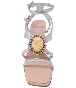 High-heeled sandal made in Italy with an open toe, strappy upper, and sculptural ankle strap secured by floral-shaped accents. Features a raised cameo embellishment with crystal trim on the instep. Presented from multiple angles against a clean background