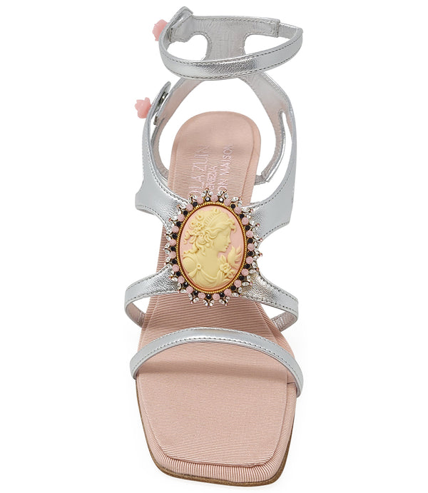 High-heeled sandal made in Italy with an open toe, strappy upper, and sculptural ankle strap secured by floral-shaped accents. Features a raised cameo embellishment with crystal trim on the instep. Presented from multiple angles against a clean background