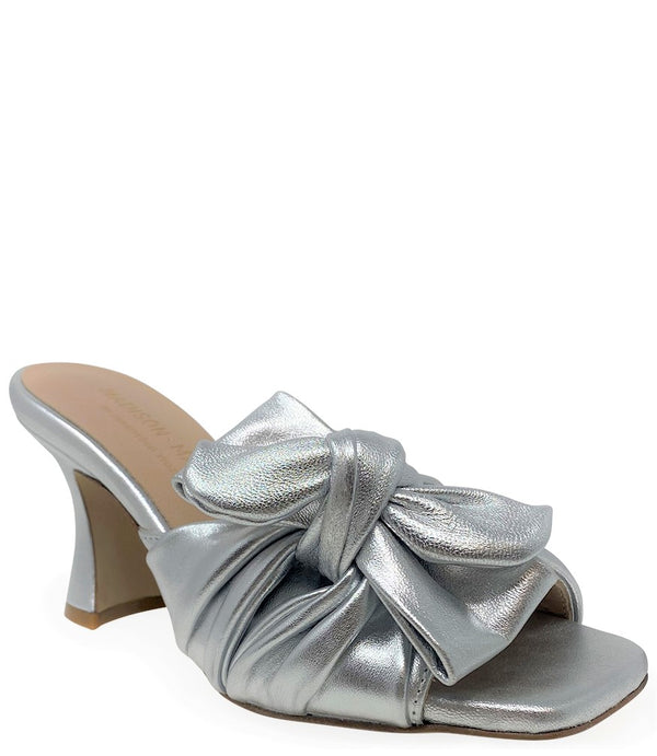 Open-toe mule handcrafted in Italy, featuring a metallic finish, wide vamp with a twisted bow detail, and a flared heel. Shown from multiple angles against a clean background